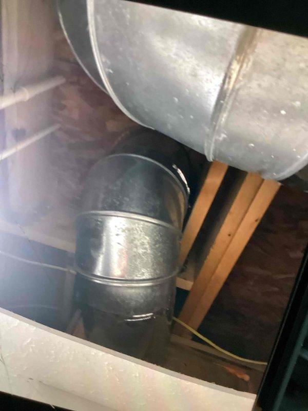 Responded to customer complaint of water dripping and ceiling staining. Upon inspection, discovered excessive condensation forming on supply air duct in attic space. Customer had already opened drywall to expose affected ductwork. Inspected galvanized metal supply duct and elbow fittings in attic cavity, noting condensation accumulation on exterior duct surfaces. Photographed existing ductwork installation showing uninsulated metal ducts in contact with unconditioned attic air, which is causing temperature differential and resulting condensation issues. Assessed surrounding wooden framing and building materials for moisture damage. Provided customer with repair options to address condensation problem, including duct insulation upgrades and proper vapor barrier installation to prevent future moisture accumulation and ceiling damage.