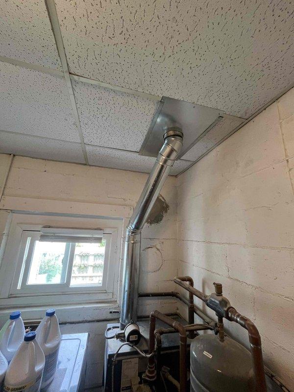 Completed return visit for previously sold HVAC installation work in mechanical room. Installed stainless steel flue pipe system with proper ceiling penetration and flashing, routing exhaust vent vertically through drop ceiling. Connected copper supply and return piping to heating equipment, including wall-mounted expansion tank with appropriate valves and fittings.
