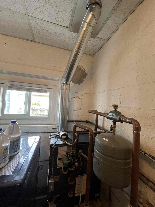 Completed return visit for previously sold HVAC installation work in mechanical room. Installed stainless steel flue pipe system with proper ceiling penetration and flashing, routing exhaust vent vertically through drop ceiling. Connected copper supply and return piping to heating equipment, including wall-mounted expansion tank with appropriate valves and fittings.