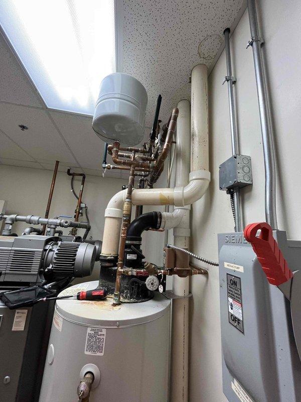 Conducted on-site assessment of existing gas-fired water heater system to develop replacement quote. Evaluated current Ruud tank-type water heater installation, documenting unit specifications including fuel type, venting configuration, and capacity requirements. Inspected power-vented combustion system with PVC vent piping, copper supply and distribution lines, expansion tank, electrical disconnect with safety lockout, and associated plumbing connections to determine replacement specifications and scope of work for future installation.