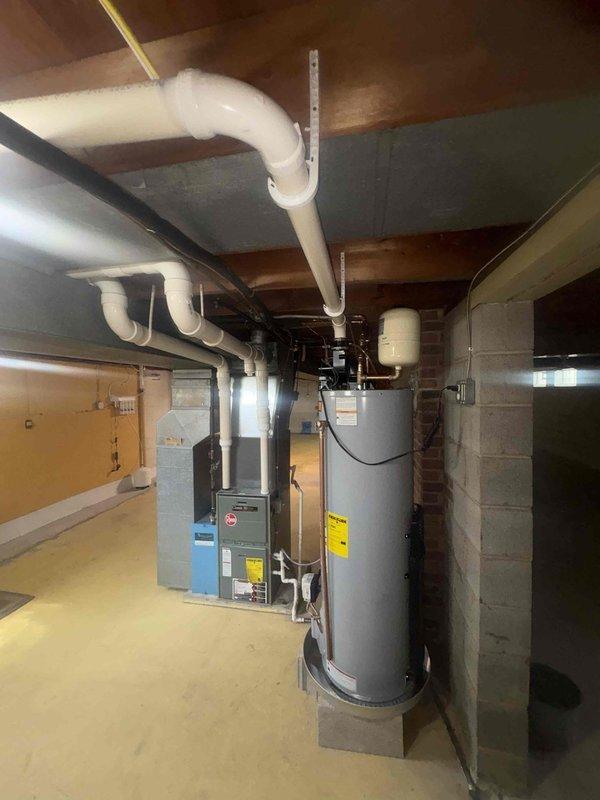 Completed water treatment system installation in residential basement utility area. New water treatment equipment was installed and integrated with existing plumbing infrastructure, including connections to the water heater and main water supply lines using copper piping and appropriate fittings to ensure proper water flow and treatment throughout the home.