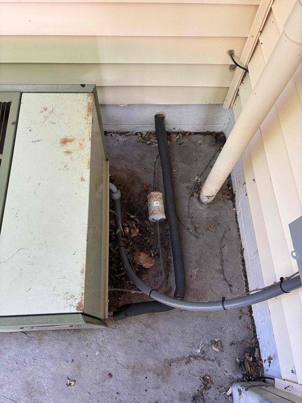 Conducted comprehensive HVAC system assessment for equipment replacement estimate. Documented existing thermostat configuration, revealing wall-mounted digital programmable unit with exposed internal components including circuit board, wiring terminals, and battery backup system. Evaluated exterior HVAC equipment location at building foundation, noting weathered concrete pad, utility connections, and existing refrigerant line routing along exterior wall. Assessment identified aging infrastructure requiring replacement to restore system efficiency and reliability.