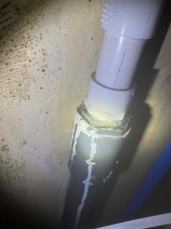 Responded to water leak at PEX pipe fitting connected to Rheem water softener system. Upon arrival, identified active moisture accumulation at pipe coupling where white PVC transitions through floor penetration. Verified leak location at metal fitting connection point with visible water pooling around base. Conducted humidity assessment of surrounding area, measuring 45% relative humidity to evaluate potential moisture damage to adjacent surfaces. Repaired leaking fitting connection and confirmed system integrity upon completion.
