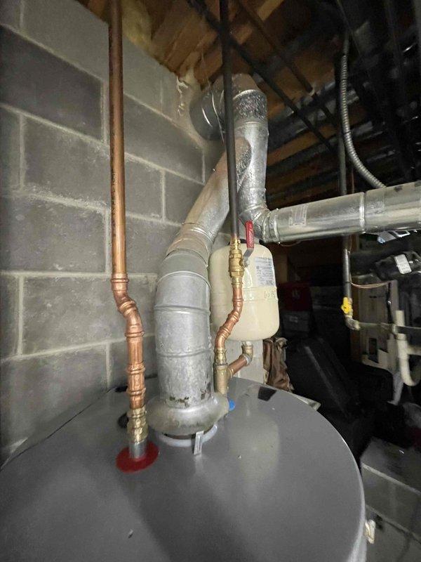 Completed installation of 50-gallon electric Ruud water heater in basement utility room. Unit was positioned on drain pan for leak protection, with copper supply lines connected to inlet and outlet ports, thermal expansion tank installed on cold water line, and proper venting system configured. All connections were secured with brass fittings, pressure relief valve installed per code requirements, and electrical connections completed to power the unit.