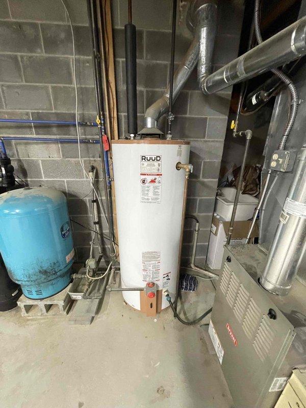 Completed installation of 50-gallon electric Ruud water heater in basement utility room. Unit was positioned on drain pan for leak protection, with copper supply lines connected to inlet and outlet ports, thermal expansion tank installed on cold water line, and proper venting system configured. All connections were secured with brass fittings, pressure relief valve installed per code requirements, and electrical connections completed to power the unit.