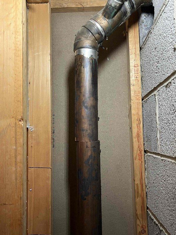 Completed follow-up repair on vertical plumbing stack installation in basement wall cavity. Replaced deteriorated metal pipe section with new white PVC piping system, including proper elbow fittings and secure mounting straps to wooden framing. Connected new PVC section to existing metal stack using appropriate transition coupling, ensuring proper alignment and structural support throughout the vertical run.