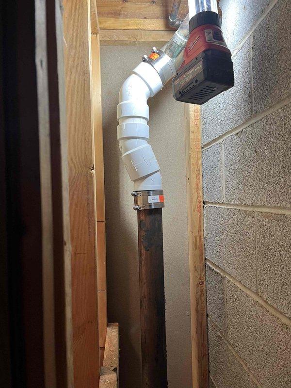 Completed follow-up repair on vertical plumbing stack installation in basement wall cavity. Replaced deteriorated metal pipe section with new white PVC piping system, including proper elbow fittings and secure mounting straps to wooden framing. Connected new PVC section to existing metal stack using appropriate transition coupling, ensuring proper alignment and structural support throughout the vertical run.