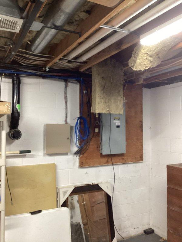 Performed comprehensive HVAC estimate for air conditioning system replacement in residential property with multiple units including in-law suite. Evaluated existing 1992 AC unit located in basement mechanical room, noting system age exceeding typical service life expectancy. Assessed current installation configuration including air handler unit, ductwork connections with black flexible ducts and metallic flexible ducting, and integration with existing electrical panels and utility infrastructure. Documented equipment location, access points, and surrounding mechanical systems to determine replacement specifications and installation requirements for new system.