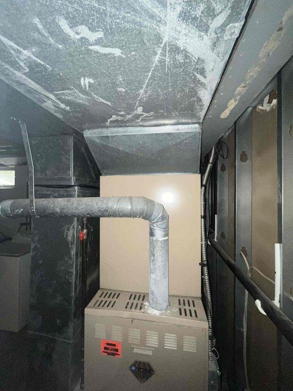 Assessed existing HVAC system in basement with water damage present. Evaluated 27-year-old air conditioning unit determined to be non-operational. Inspected furnace and ductwork configuration, noting silver metal supply duct with curved transition and existing ventilation layout. Documented water staining on ceiling and walls affecting installation area. Provided estimate for budget-friendly replacement system to address failed AC unit and accommodate existing infrastructure while accounting for moisture-damaged environment.