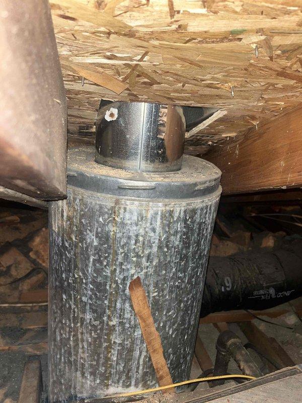 Responded to service call for B-vent condensate dripping issue. Upon inspection, found moisture accumulation on the galvanized B-vent connector beneath the floor structure, indicating improper venting or condensation concerns with the natural draft appliance. Documented existing conditions showing weathered B-vent assembly with visible moisture exposure and corrosion patterns on the galvanized surface. Inspected furnace and water heater installation in utility room to assess venting configuration and identify source of condensate formation.