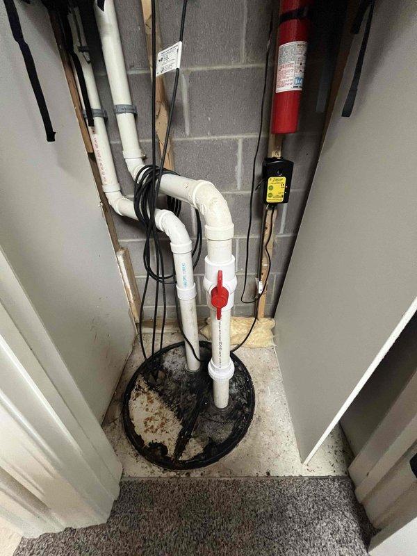 Responded to sump pump alarm activation in utility closet. Upon inspection, found sump pump system with basin installed in concrete floor with PVC discharge piping and check valve assembly. Verified pump operation, tested float switch mechanism, and confirmed proper electrical connections. Cleared debris from basin and ensured adequate drainage. System returned to normal operation with alarm silenced and pump cycling correctly.
