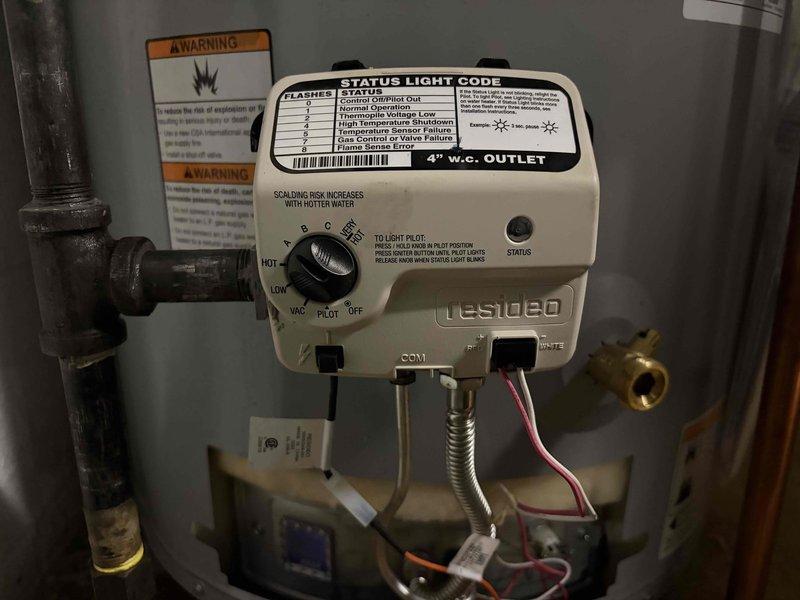 Responded to emergency water leak at four-year-old gas water heater with Testoco control unit. Upon inspection, discovered water pooling on top of tank surface near recently installed components. Identified leak source from connection point associated with copper piping and brass fittings at top of unit. Documented conditions with photographs showing moisture accumulation on flat top surface and blue push-fit connector at pipe junction. Assessed control unit functionality and verified proper operation settings. Addressed leak at attachment point to prevent further water damage.