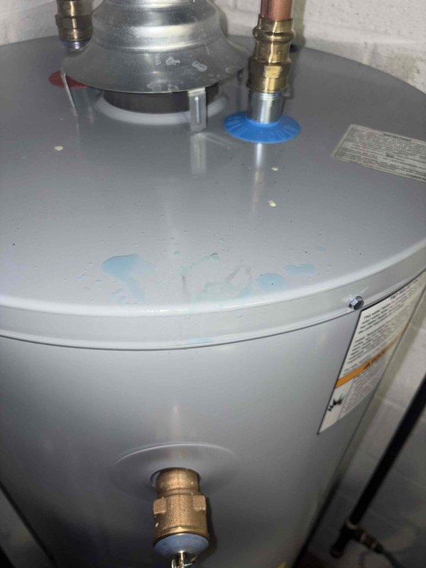 Responded to emergency water leak at four-year-old gas water heater with Testoco control unit. Upon inspection, discovered water pooling on top of tank surface near recently installed components. Identified leak source from connection point associated with copper piping and brass fittings at top of unit. Documented conditions with photographs showing moisture accumulation on flat top surface and blue push-fit connector at pipe junction. Assessed control unit functionality and verified proper operation settings. Addressed leak at attachment point to prevent further water damage.