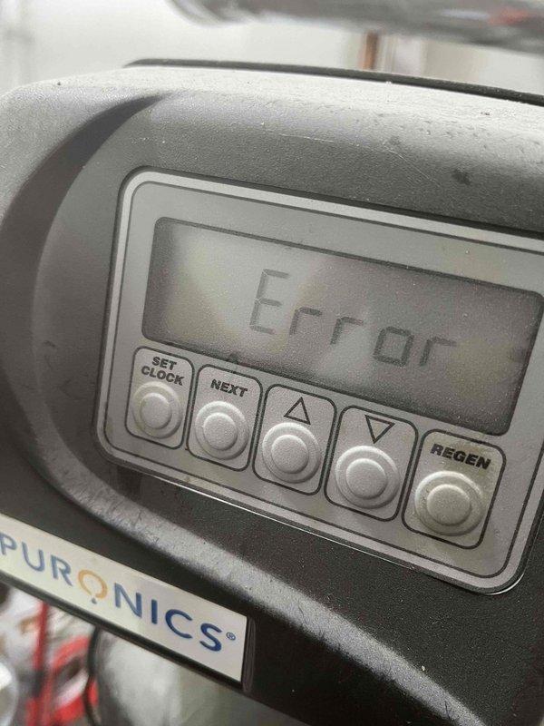 Responded to service call for discolored water with sediment in newly occupied residence. Upon inspection, found existing Puronics water treatment system displaying error code on control panel. Collected water samples showing significant discoloration and sediment contamination compared to treated water standard. Diagnosed system malfunction preventing proper filtration and regeneration cycle, requiring troubleshooting of control unit and assessment of filter media condition to restore water quality.