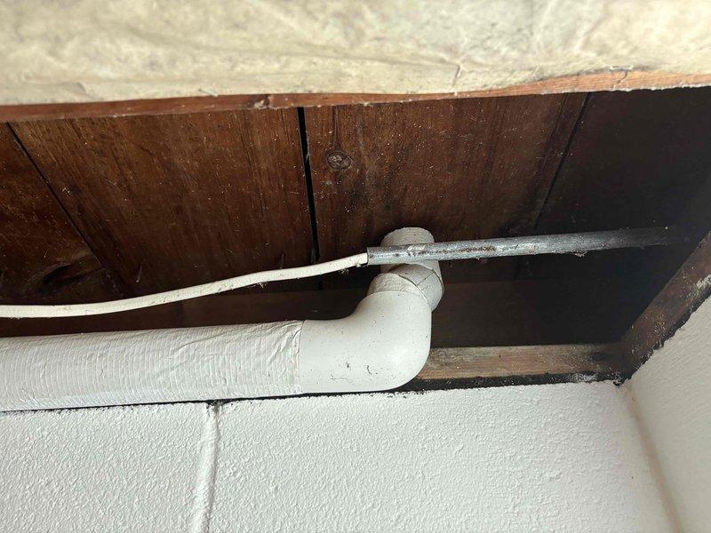 Completed site inspection of basement utility area to assess HVAC infrastructure and conditions. Documented exposed ceiling joists with fiberglass insulation installation, noting areas where batting material has sagged and requires repositioning for optimal thermal efficiency. Photographed PVC drainage lines running through wooden framing along concrete block walls to verify proper routing and clearances for future HVAC equipment considerations.