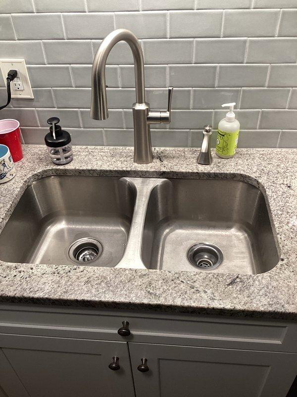 # Emergency Plumbing Service - Standing Water Resolution

Responded to emergency call for standing water in residence. Upon arrival, assessed forty-year-old plumbing system experiencing drainage issues causing water accumulation within the home. Performed diagnostic inspection of kitchen sink drainage system and associated plumbing connections.

Inspected double-basin stainless steel sink installation with contemporary fixtures including pull-down faucet and soap dispenser. Examined drain assemblies in both basins and traced drainage lines to identify blockage source. Evaluated water heater connections and shut-off valve assembly, noting brass elbow fitting with PEX piping configuration to ensure no related leaks contributing to standing water issue.

Successfully cleared clogged drain obstruction, restoring proper water flow and eliminating standing water condition. Tested both sink basins for proper drainage function and verified all connections remained secure with no active leaks. 