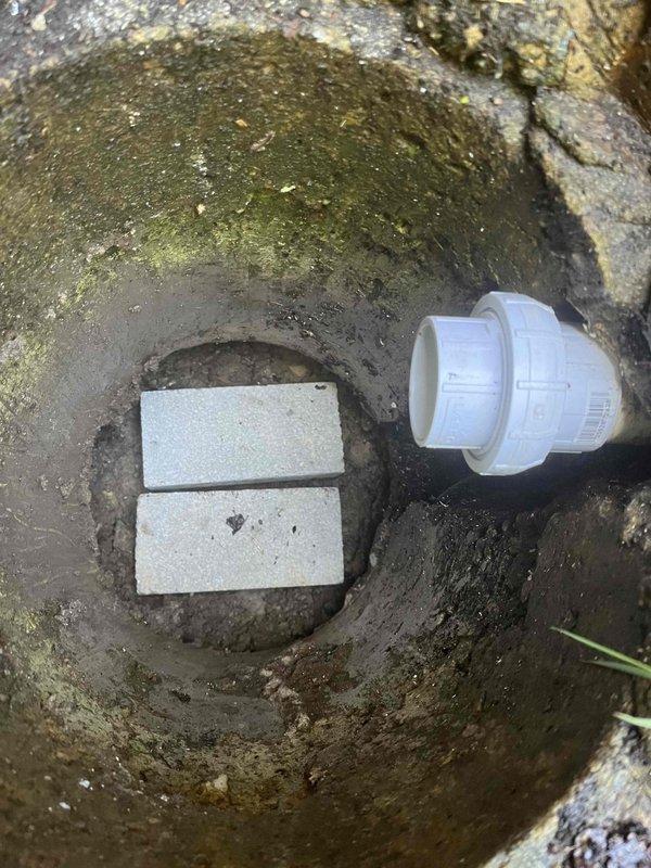 Responded to emergency call for sump pump failure in a forty-year-old residential property. Upon arrival, accessed the sump basin and found the existing pump had failed, leaving the system inoperative and the home vulnerable to water damage. The basin showed significant age-related deterioration with heavy staining, algae growth, and mineral deposits throughout the concrete structure. 

Removed the failed pump unit from the circular concrete sump pit and cleared accumulated debris from the basin floor. Inspected the discharge piping system, including the white PVC coupling and associated plumbing connections for proper function and structural integrity. Positioned concrete blocks at the basin base to provide stable support for the replacement pump installation. 

Installed new sump pump unit with proper electrical connections and verified secure positioning within the basin. Connected discharge assembly to existing white PVC piping system and tested all fittings for water-tight seals. 
