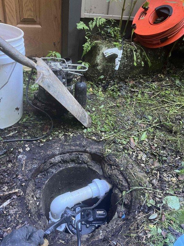 Responded to emergency call for sump pump failure in a forty-year-old residential property. Upon arrival, accessed the sump basin and found the existing pump had failed, leaving the system inoperative and the home vulnerable to water damage. The basin showed significant age-related deterioration with heavy staining, algae growth, and mineral deposits throughout the concrete structure. 

Removed the failed pump unit from the circular concrete sump pit and cleared accumulated debris from the basin floor. Inspected the discharge piping system, including the white PVC coupling and associated plumbing connections for proper function and structural integrity. Positioned concrete blocks at the basin base to provide stable support for the replacement pump installation. 

Installed new sump pump unit with proper electrical connections and verified secure positioning within the basin. Connected discharge assembly to existing white PVC piping system and tested all fittings for water-tight seals. 