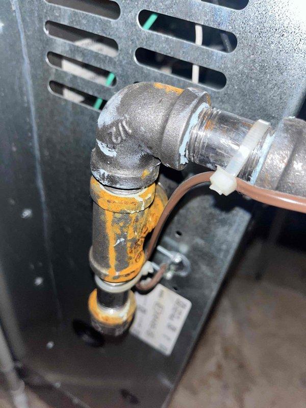 Responded to service call for air conditioning unit with reported water leakage. Upon inspection, discovered active condensation on evaporator coil assembly and drainage system components. Examined condensate drain line connections, including elbow fitting and copper piping, noting normal moisture accumulation on coil fins consistent with system operation. Verified proper drainage function and confirmed unit was cooling effectively with no blockages detected in the drain system.