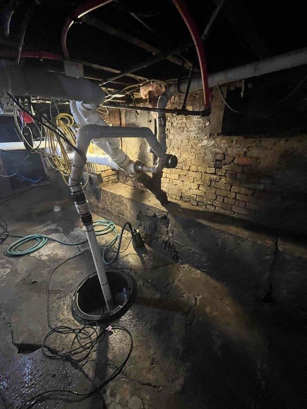 Responded to emergency flooding situation in basement caused by grease-clogged lateral sewer line. Upon arrival, confirmed municipal main line was clear per city inspection, isolating issue to property's lateral connection. Basement showed extensive sewage backup with standing water containing human waste throughout the space.

Assessed the affected area which included exposed brick walls, concrete flooring, and mechanical systems. Water accumulation was visible across multiple sections of the basement floor, creating hazardous conditions around existing plumbing infrastructure and electrical components. 

Deployed professional-grade work lighting to properly evaluate the extent of contamination and identify access points for remediation. Located the source of the blockage in the lateral line where significant grease buildup had created a complete obstruction, preventing proper drainage and causing sewage to back up into the basement through floor drains and low-lying plumbing fixtures