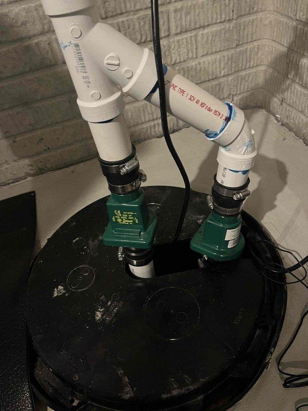 Completed comprehensive inspection of dual-pump sump system. Evaluated submersible pump operation, discharge piping configuration with white PVC and black flexible hoses, and overall basin condition. Documented significant sediment accumulation and debris in standing water at basin floor, both green-colored pumps operational and properly secured with metal clamps and strapping, and all connections intact. Photographed system for service records showing typical wear patterns consistent with regular use.