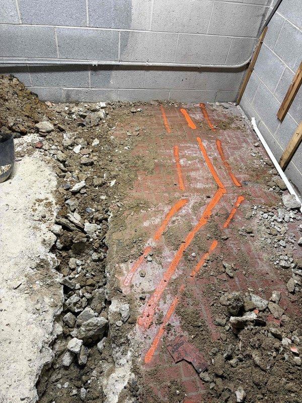 Returned to property to continue exterior clean-out installation previously sold. Excavated basement floor and installed parallel runs of white PVC drainage piping in prepared trenches, ensuring proper slope and alignment using leveling tools. Work is currently on hold pending completion of restoration activities by fire and water damage remediation company before final backfill and concrete restoration can be completed.