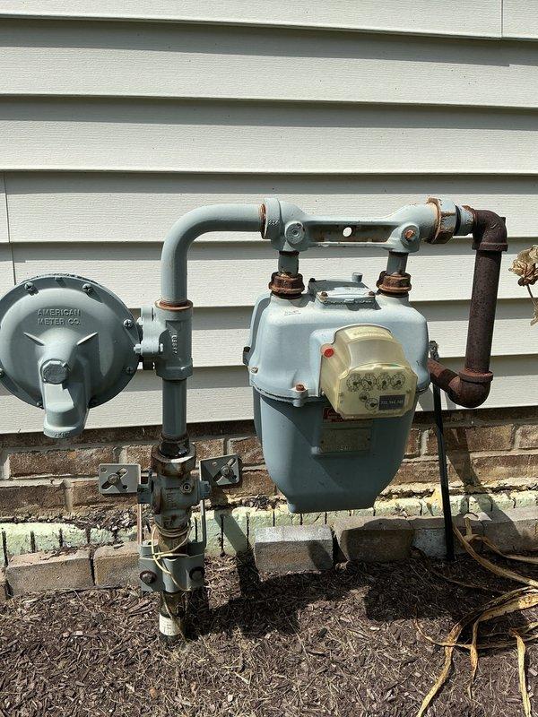 Installed new gas line to accommodate gas dryer installation in residence that previously only had electric hookup. Ran copper piping through basement ceiling joists with proper mounting brackets and support hardware to ensure secure installation and code compliance. Inspected existing natural gas meter and pressure regulator system on exterior of building, noting corrosion present on older pipe connections. Completed gas line rough-in work to prepare for dryer connection, with additional faucet replacement work to be scheduled pending availability of replacement fixtures.