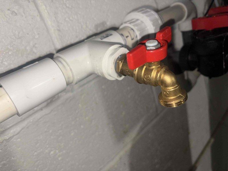 Responded to emergency call for newly installed well pump system failure that caused water discharge into basement. Upon arrival, assessed damaged piping connections and identified compromised PVC joints that resulted in system breach. Shut off water supply, drained affected lines, and inspected full extent of leak damage. Reinstalled and properly secured white PVC water supply piping with correct fittings and couplings. Replaced brass hose bib assembly with 90-degree elbow configuration and installed red-handled shut-off valve for system isolation. Verified all pipe connections were properly sealed and pressure-tested system to ensure no additional leaks. Confirmed proper operation of well pump system and restored water service to residence.