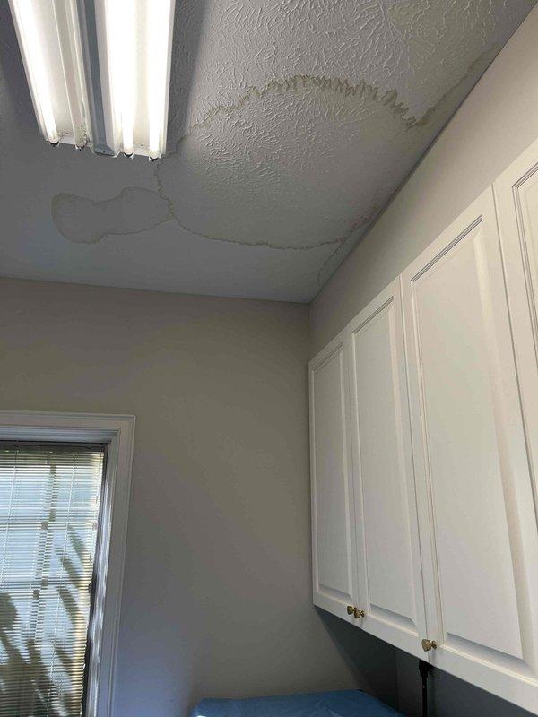 Responded to water leak originating from upstairs bathroom causing visible ceiling damage in laundry room below. Upon inspection, identified active leak source at toilet tank connection in bathroom above affected area. Documented extensive water staining and discoloration on laundry room ceiling with brownish-gray patches indicating prolonged moisture intrusion. Inspected toilet fixture including tank, flush mechanism, and supply line connections. Addressed leak at point of origin to prevent further water damage to ceiling and surrounding structures.