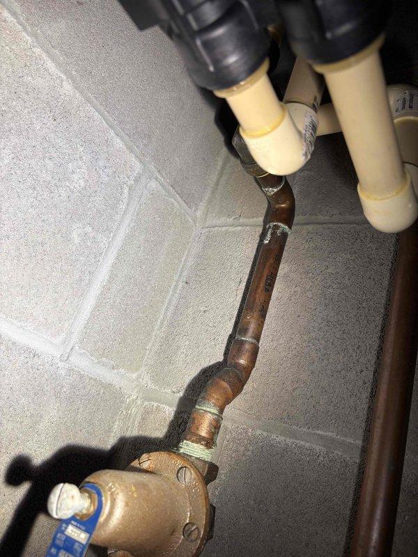 Responded to active water leak with water penetrating through ceiling from upper level bathroom. Performed initial assessment and created access opening in ceiling to investigate source and extent of water intrusion. Inspected exposed plumbing system including mixed copper and PEX piping with brass valves mounted on concrete block wall. Water infiltration continues from adjacent bathroom area. Investigation incomplete pending customer confirmation to schedule follow-up visit for comprehensive diagnosis, leak source identification, and repair quotation.