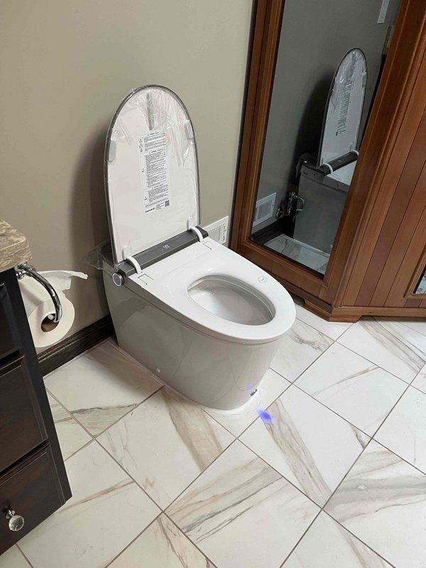 Completed installation of customer-supplied bidet toilet system in residential bathroom. Installed modern elongated bowl toilet with integrated bidet seat featuring electronic control panel. Secured all mounting hardware, connected water supply lines, and tested bidet functionality. Verified proper flush operation, checked for leaks at all connection points, and ensured electronic controls were functioning correctly. Toilet installed on existing marble-style tile flooring with proper wax ring seal and floor bolts. All components operating as designed upon completion.