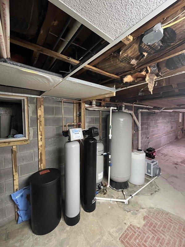 Completed installation of comprehensive water treatment system in basement mechanical room. Installed series of five treatment tanks including softener units and filtration vessels with interconnecting PVC piping and proper drainage connections. Mounted equipment on concrete floor with appropriate spacing for maintenance access. Established electrical connections via dedicated outlet box with armored conduit for system power supply. Verified all plumbing connections for proper flow direction and leak-free operation. System commissioned and tested for functionality.