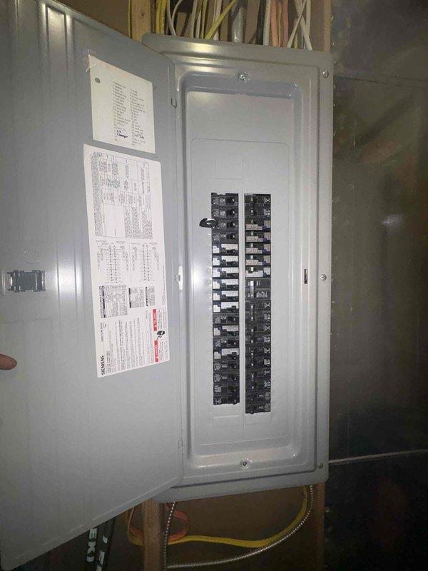 Completed tankless water heater installation with electrical panel integration and proper circuit protection. Installed dedicated electrical circuit breakers in the main panel box to support the unit's power requirements, ensuring compliance with manufacturer specifications and electrical code standards. Mounted the tankless water heater control panel on painted brick wall with copper supply lines connected, verified level installation, and confirmed all connections were secure and operational.