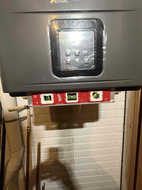 Completed tankless water heater installation with electrical panel integration and proper circuit protection. Installed dedicated electrical circuit breakers in the main panel box to support the unit's power requirements, ensuring compliance with manufacturer specifications and electrical code standards. Mounted the tankless water heater control panel on painted brick wall with copper supply lines connected, verified level installation, and confirmed all connections were secure and operational.