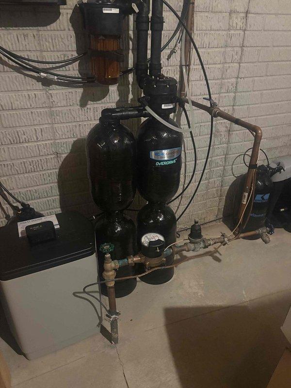 Responded to emergency call for catastrophic gas water heater failure that resulted in tank rupture through drywall and active flooding. Immediately shut off gas supply and water supply to compromised unit to prevent further damage and ensure safety. Documented equipment failure including measurements of damaged 24-inch diameter cylindrical water heater tank and photographed existing pressure tank system with dual black cylindrical vessels, copper piping, pressure gauge, and associated plumbing components. Customer contacted insurance company for claim processing due to extent of property damage from water heater explosion.