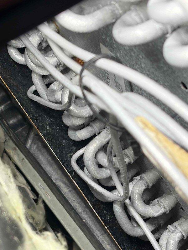 Responded to recurring AC alarm on 5-year-old outdoor unit. Upon inspection, discovered extensive frost and ice buildup on evaporator coil assembly, indicating restricted airflow or refrigerant issue. Found insulated refrigerant lines properly secured but system experiencing freezing condition similar to previous service call. Documented frost accumulation covering serpentine coil pattern throughout heat exchanger. Photographed affected components showing thick white frost coating on coil surfaces and refrigerant line routing. System requires further diagnosis to determine root cause of recurring freeze-up condition, likely related to airflow restriction, refrigerant charge imbalance, or metering device malfunction that was not fully resolved during previous repair.