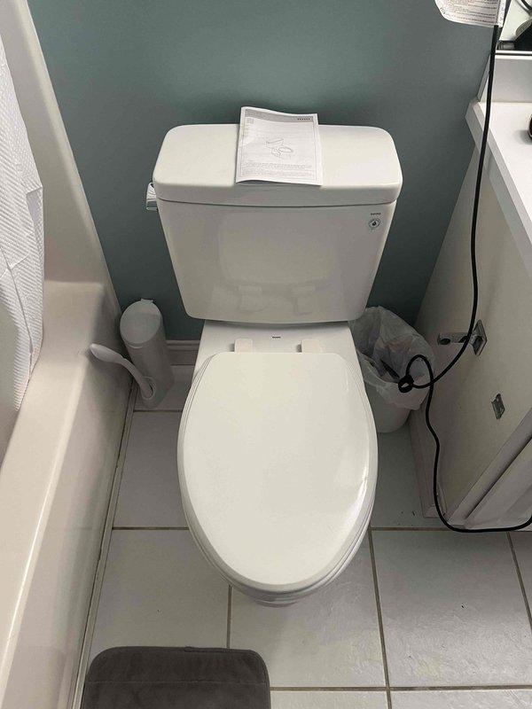 Completed full toilet replacement in residential bathroom. Removed existing two-piece toilet unit, installed new white porcelain two-piece toilet with standard flush mechanism, connected flexible braided water supply line to wall shutoff valve, set toilet with new wax ring seal, secured unit to floor flange, tested for proper operation and verified no leaks at connections or base.