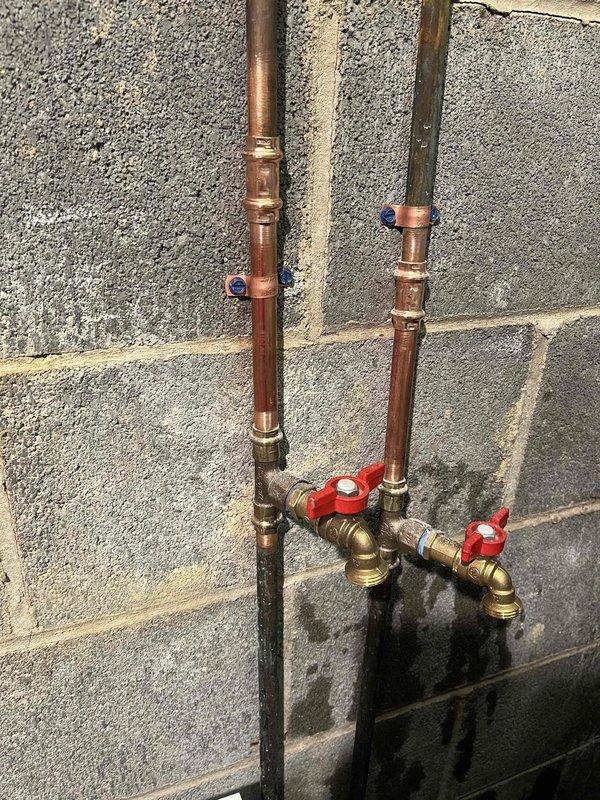 Replaced defective shut-off valves in basement water supply system. Installed new brass ball valves with red handles on parallel copper supply lines mounted to concrete block wall, ensuring proper shutoff capability for the building's water distribution system.