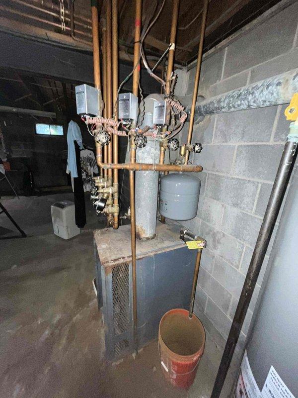 Responded to service call for water leak on aging furnace system in basement. Upon arrival, inspected 20+ year old heating unit and associated plumbing connections. Identified source of leak at copper piping connections to boiler unit. Examined red circulation pump, expansion tank, and water heater connections for additional moisture or compromised fittings. Documented existing conditions of mechanical systems including oxidized copper piping, brass valves, and plumbing manifold. Placed collection bucket beneath active leak point to prevent floor damage. Assessed overall condition of heating system and associated components. Due to age of equipment and extent of deterioration observed in piping and connections, recommended evaluation for system replacement versus repair options. Provided customer with photographic documentation of equipment condition and leak location for review and decision on next steps.