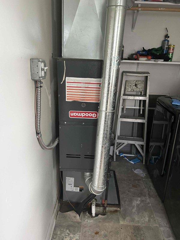 # HVAC Service Report - No Cooling Issue

Responded to no-cooling call on residential Goodman HVAC system that had developed rattling sounds before ceasing operation. Upon arrival, performed diagnostic assessment of furnace and air handler unit located in garage utility area. Inspected electrical connections, junction box, and flexible conduit for loose components or wiring issues that could cause rattling and system shutdown. Checked thermostat communication and power supply to unit. Examined air handler for mechanical failures, loose blower components, or debris causing abnormal noise. Verified ductwork connections and assessed overall system operation. Documented equipment condition through photographic records showing furnace installation, ductwork configuration, and electrical connections for service history.
