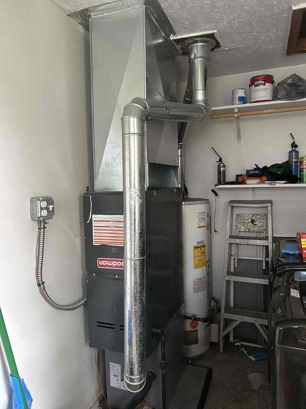 # HVAC Service Report - No Cooling Issue

Responded to no-cooling call on residential Goodman HVAC system that had developed rattling sounds before ceasing operation. Upon arrival, performed diagnostic assessment of furnace and air handler unit located in garage utility area. Inspected electrical connections, junction box, and flexible conduit for loose components or wiring issues that could cause rattling and system shutdown. Checked thermostat communication and power supply to unit. Examined air handler for mechanical failures, loose blower components, or debris causing abnormal noise. Verified ductwork connections and assessed overall system operation. Documented equipment condition through photographic records showing furnace installation, ductwork configuration, and electrical connections for service history.