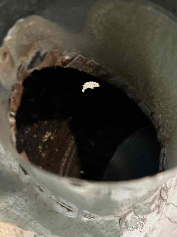 Responded to service call for hydronic boiler system with corroded vent pipe. Upon inspection, discovered severe deterioration of vent pipe extending to wall penetration point, with significant corrosion visible at pipe opening and rim showing rust-colored oxidation and material breakdown. Documented existing conditions including compromised pipe integrity, crumbling edges, and internal buildup. Observed structural concerns at wall junction where vent pipe meets masonry, noting cracked cinder block and deteriorated joint material. Photographed damage for assessment and provided recommendations for vent pipe replacement and evaluation of chimney liner condition before proceeding with repairs.