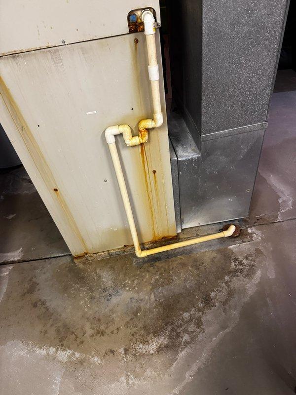 Responded to service call for water accumulation beneath air handler unit. Upon inspection, discovered active condensate drainage issue with significant water staining on floor and rust-colored discharge marks along PVC condensate drain piping. Documented existing moisture damage to concrete floor showing efflorescence and mineral deposits, indicating ongoing or repeated drainage problems. Photographed compromised condensate drain system with visible leakage at pipe joints and connections requiring immediate attention to prevent further water damage to basement area and potential secondary issues with HVAC equipment operation.