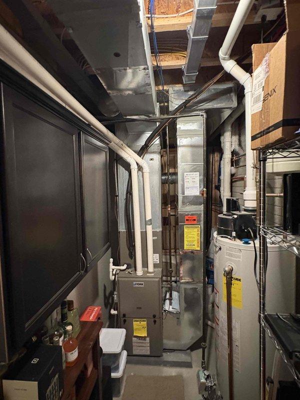 Completed comprehensive estimate for proactive replacement of 14-year-old air conditioning system and furnace located in basement mechanical room. Evaluated existing vertical furnace configuration with integrated Aprilaire humidifier, assessed current ductwork infrastructure including metal supply and return ducts, and documented white PVC drainage lines and electrical connections. Photographed equipment layout, clearances, and access points to develop accurate replacement specifications for both heating and cooling systems.