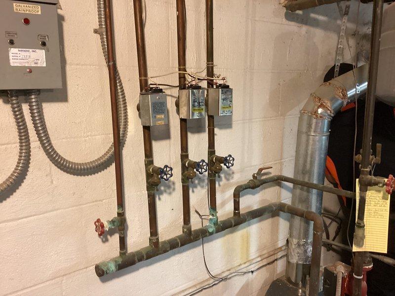 Responded to inquiry regarding corroded boiler vent pipe repair on hydronic heating system. Performed on-site inspection and documented existing conditions of mechanical room infrastructure, including copper piping with shutoff valves, pressure gauges, expansion tank, and aging plumbing components showing oxidation and patina. Assessed vent pipe corrosion extending to wall penetration point and evaluated system components for repair feasibility and liner condition determination.