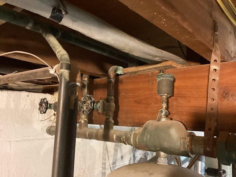 Responded to inquiry regarding corroded boiler vent pipe repair on hydronic heating system. Performed on-site inspection and documented existing conditions of mechanical room infrastructure, including copper piping with shutoff valves, pressure gauges, expansion tank, and aging plumbing components showing oxidation and patina. Assessed vent pipe corrosion extending to wall penetration point and evaluated system components for repair feasibility and liner condition determination.