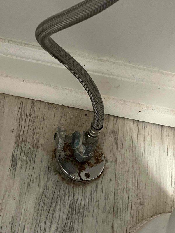 Responded to no hot water complaint at residential property. Upon arrival, accessed property through back entrance as requested. Inspected tanked water heater system and associated plumbing connections. Identified corroded water supply line mounting hardware with significant rust deterioration at wall connection point. Examined exterior hose bib and related plumbing fixtures to assess overall system condition. Documented existing corrosion on flexible supply line escutcheon and mounting plate. All findings photographed for service records. System evaluated and customer advised of observations.