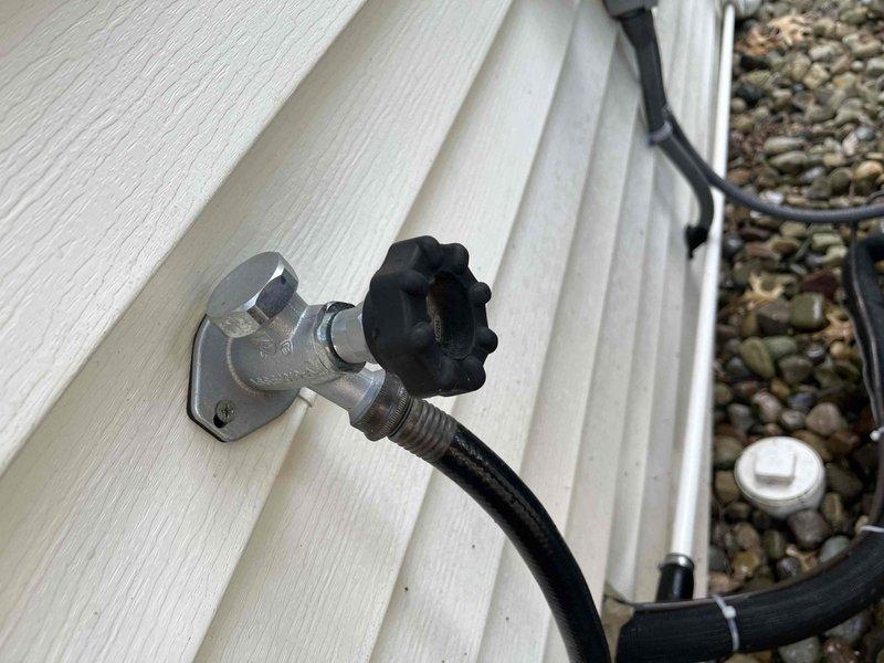 Responded to no hot water complaint at residential property. Upon arrival, accessed property through back entrance as requested. Inspected tanked water heater system and associated plumbing connections. Identified corroded water supply line mounting hardware with significant rust deterioration at wall connection point. Examined exterior hose bib and related plumbing fixtures to assess overall system condition. Documented existing corrosion on flexible supply line escutcheon and mounting plate. All findings photographed for service records. System evaluated and customer advised of observations.