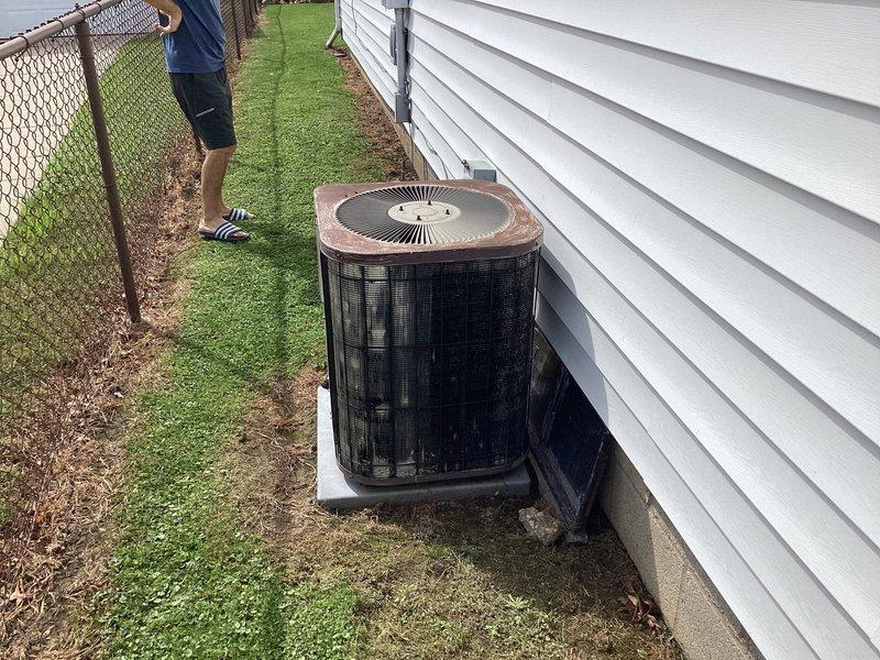 Completed HVAC system evaluation for residential property with 25+ year old furnace and air conditioning system of similar age. Both heating and cooling systems currently operational. Assessed existing cylindrical outdoor condensing unit with tan top panel positioned against home's exterior siding near chain-link fence, and evaluated interior living space for replacement equipment considerations.