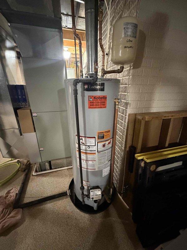 Responded to service call for 50-gallon natural gas water heater with reported leaking from top connections and water accumulation in catch basin. Upon arrival, confirmed active leak at upper plumbing connections and verified pilot light was not lit. Assessed Lochinvar unit and determined leak source required immediate attention to prevent further water damage. Instructed occupant on emergency shutdown procedure including closing cold water supply valve to tank and running hot water taps to relieve pressure in system. Documented existing conditions including expansion tank installation and copper supply line configuration for service records.